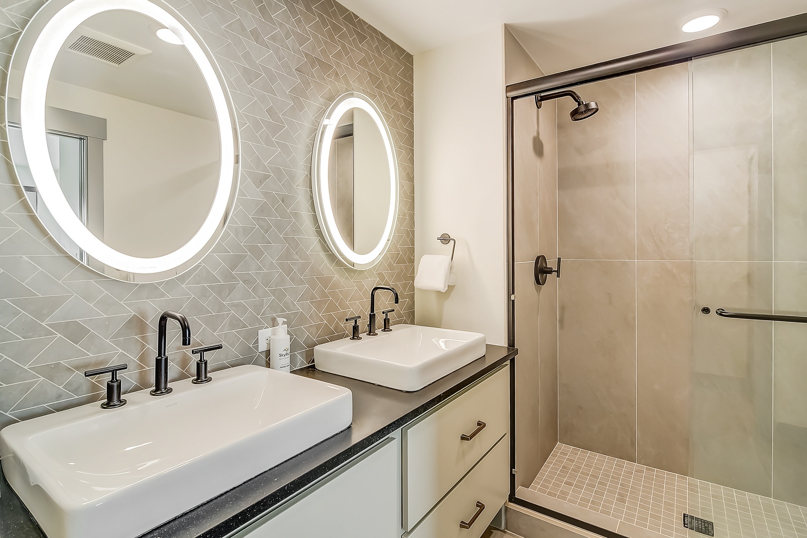Step into your beautifully appointed bathroom with elegant double vanities, illuminated mirrors, and a spacious glass-enclosed shower.
