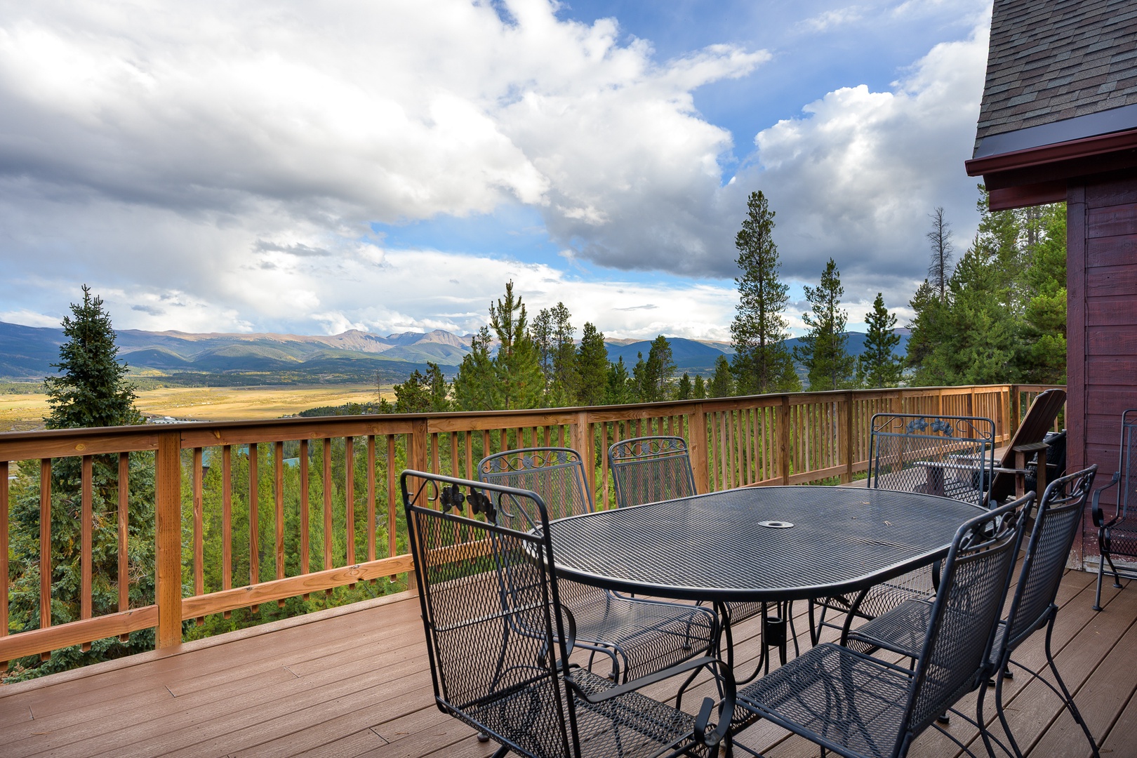 Sweeping mountain vistas frame this spacious deck, where morning coffee or evening meals become unforgettable. Pine trees and dramatic clouds create a serene backdrop for gatherings.