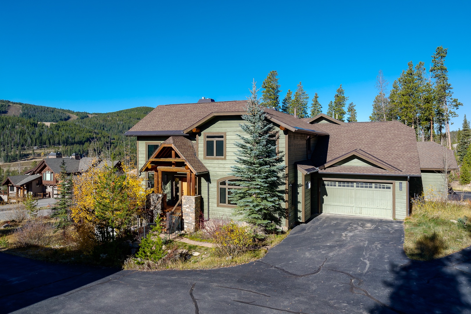 Mountain retreat featuring modern architecture with natural stone accents, surrounded by evergreen forests and autumn foliage in a peaceful alpine setting.