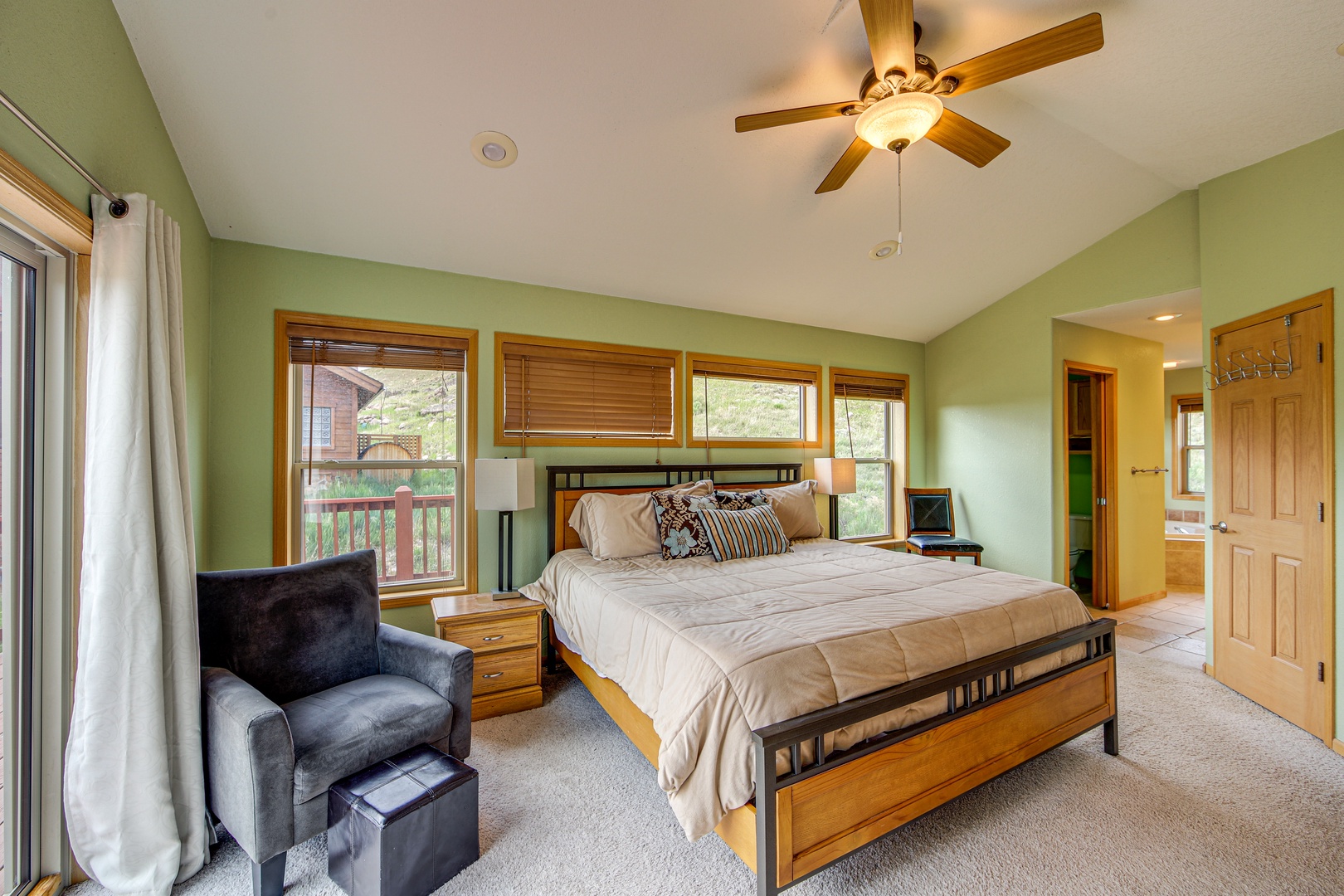 Relax in your spacious bedroom with soothing green walls, comfortable seating, and peaceful views through multiple windows.