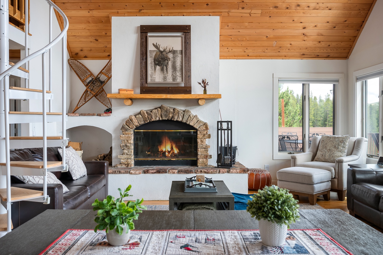 Warm up beside the stone fireplace in your open-concept living room, where a spiral staircase leads to cozy bunk beds above. Natural light pours through the windows, inviting you to relax in the countryside view.
