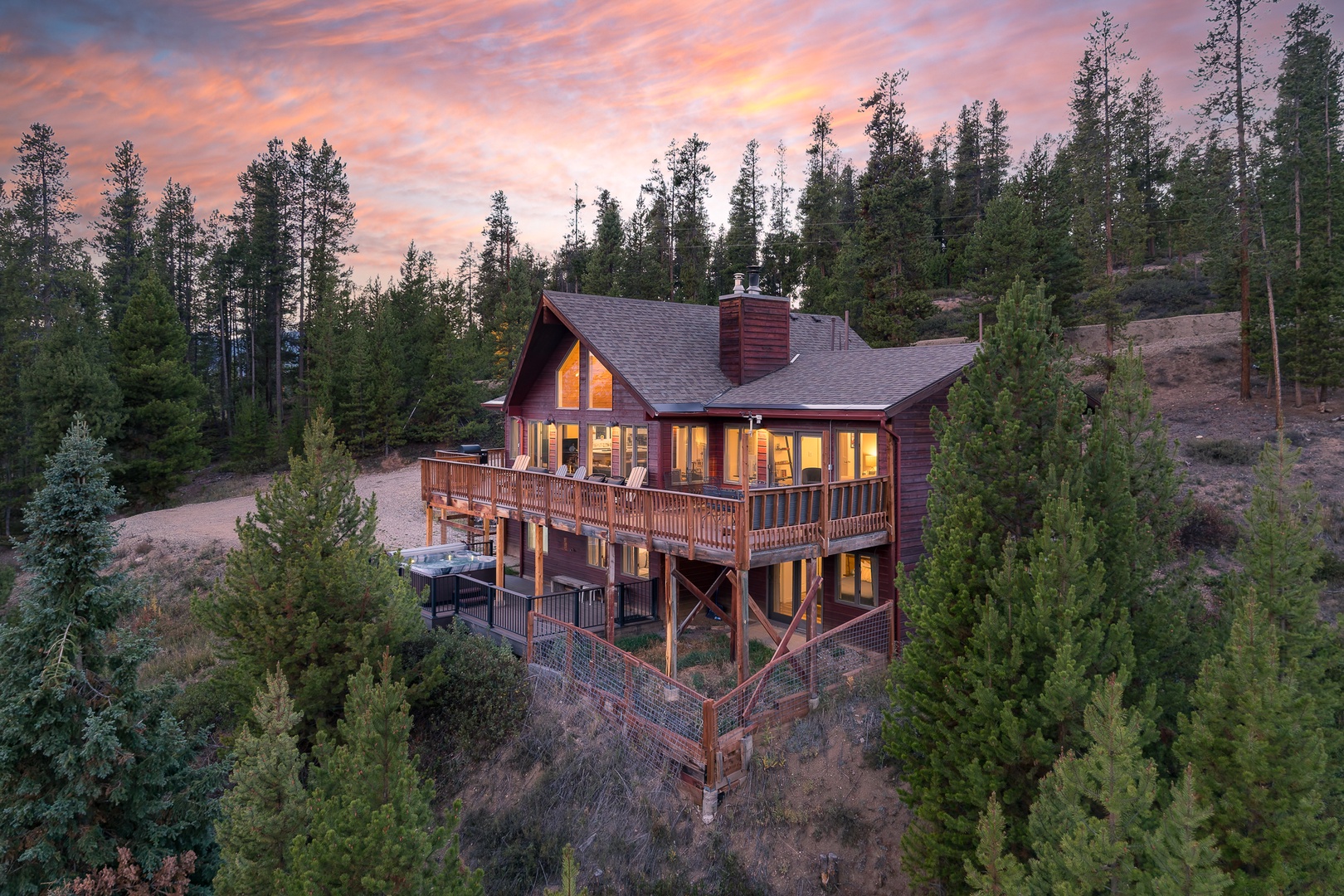 A stunning mountain cabin nestled among towering pines, glowing warmly as the sun sets over the forested landscape—your perfect retreat awaits.