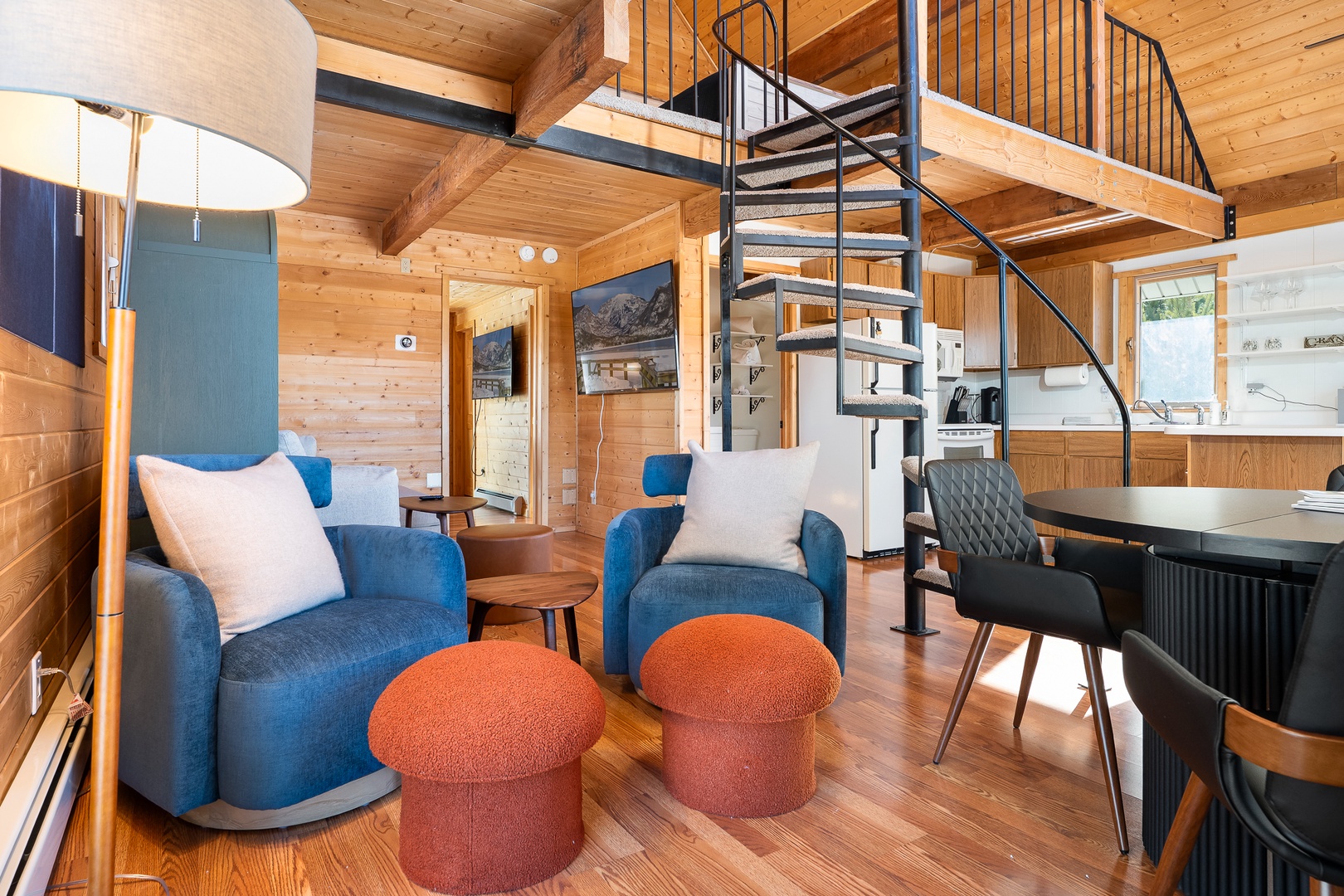 Cozy wood-paneled retreat with stylish blue armchairs and spiral staircase leading to your private loft space above.