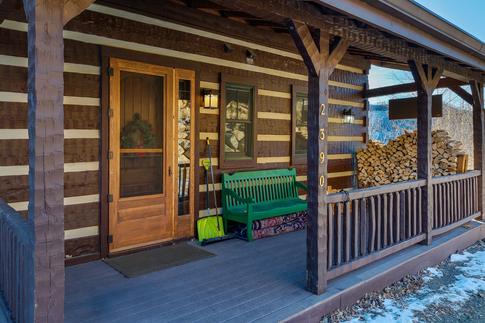 Rustic log cabin entrance with covered porch, green bench seating, and stacked firewood creating authentic mountain retreat atmosphere.