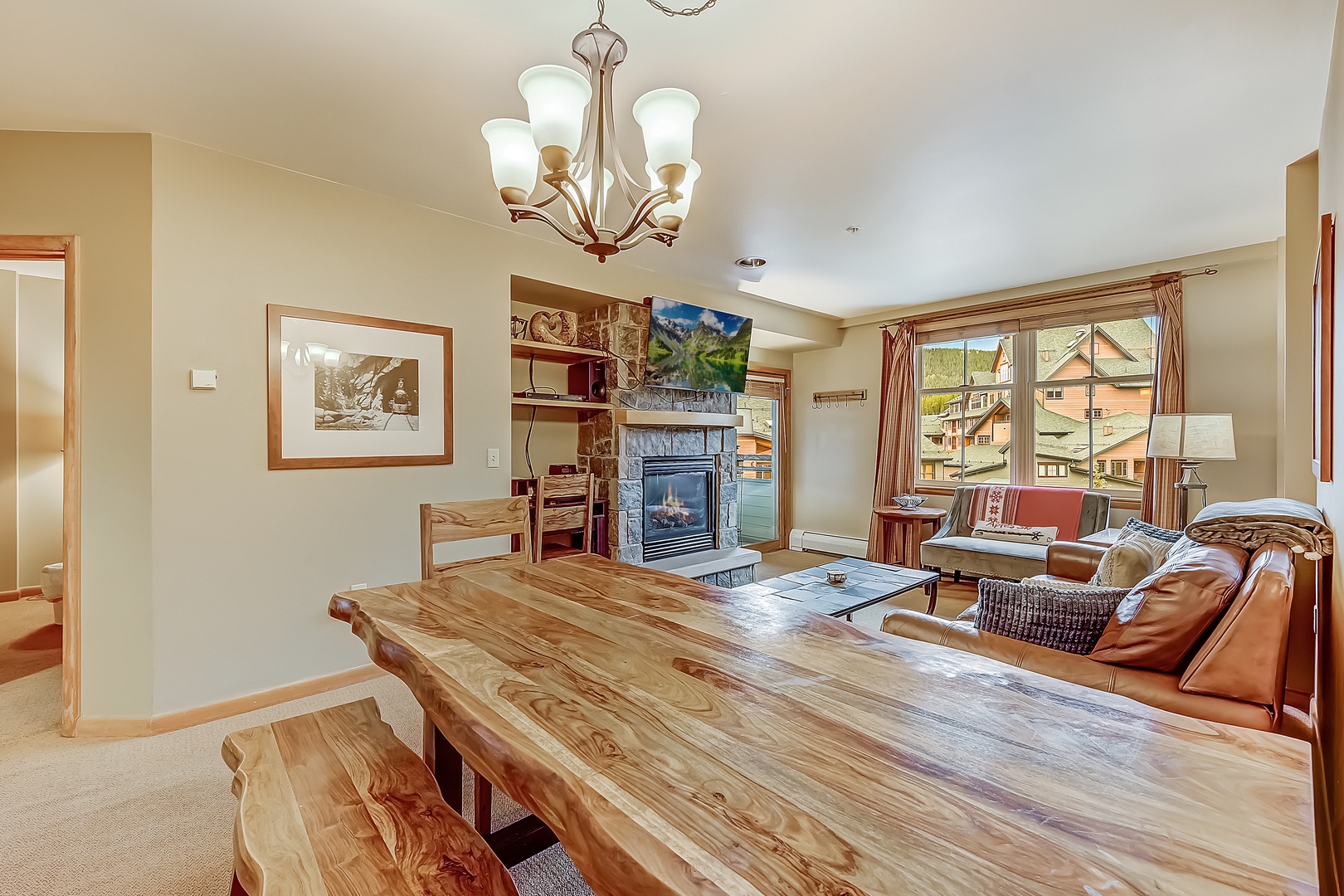 Gather around the handcrafted wood table while natural light streams through large windows, revealing surrounding neighborhood views. The cozy fireplace and leather seating invite you to unwind after a day of mountain adventures.