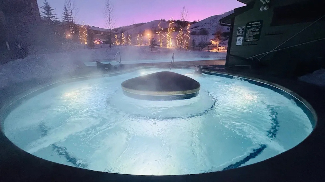 Soak in the steaming hot tub under a winter twilight sky, surrounded by snow-covered mountains and twinkling lights.