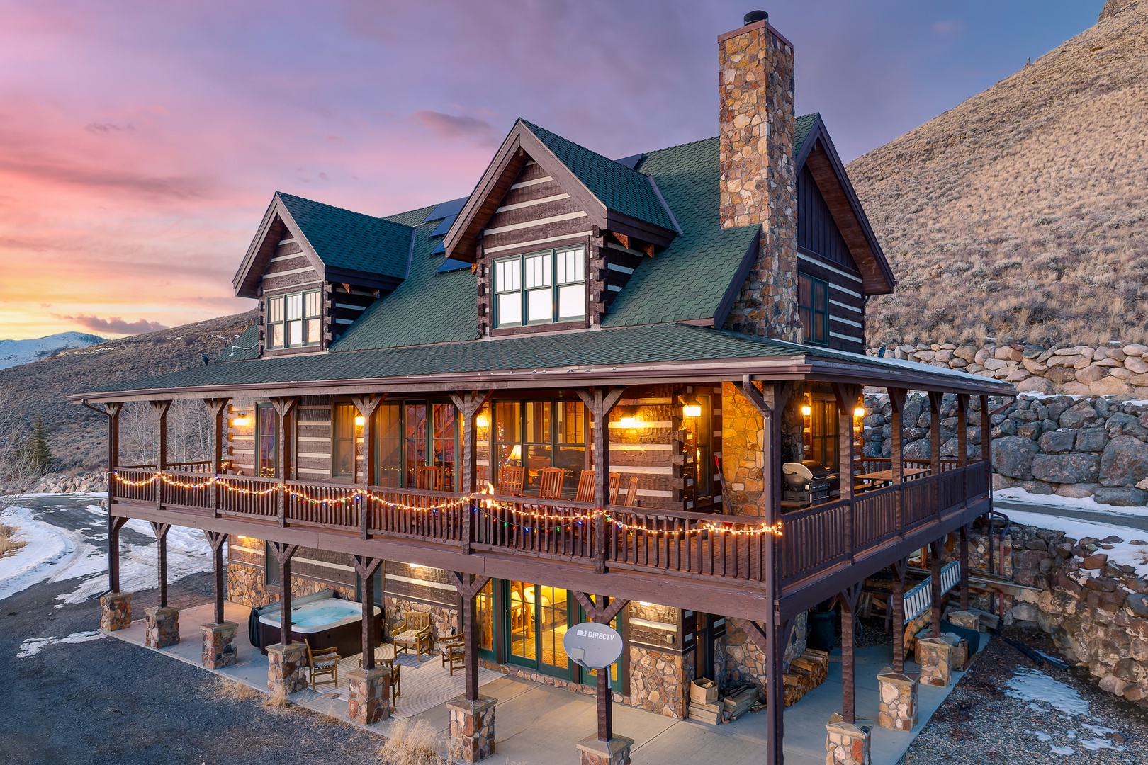 Stunning log cabin retreat nestled in the rocky mountains, featuring wraparound porche with private hot tub and firepit and vibrant sunset skies.