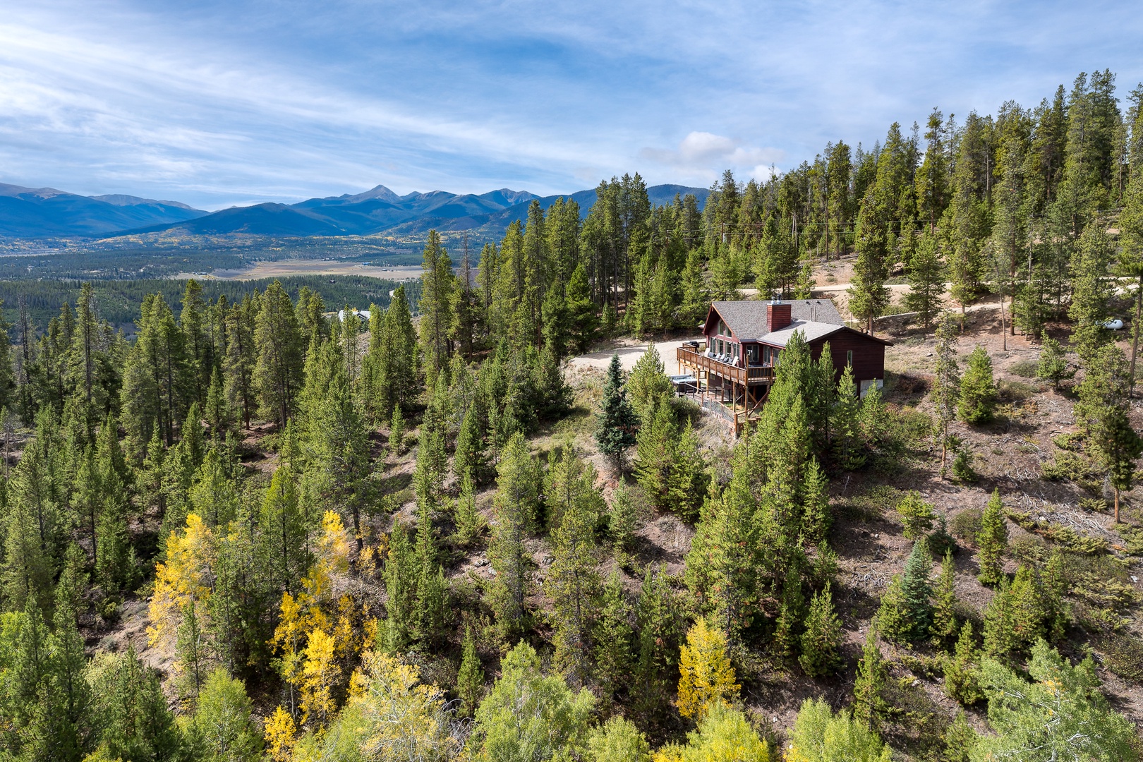 Aerial view of a mountain retreat nestled among evergreens and golden aspens, with sweeping mountain ranges visible in the distance.