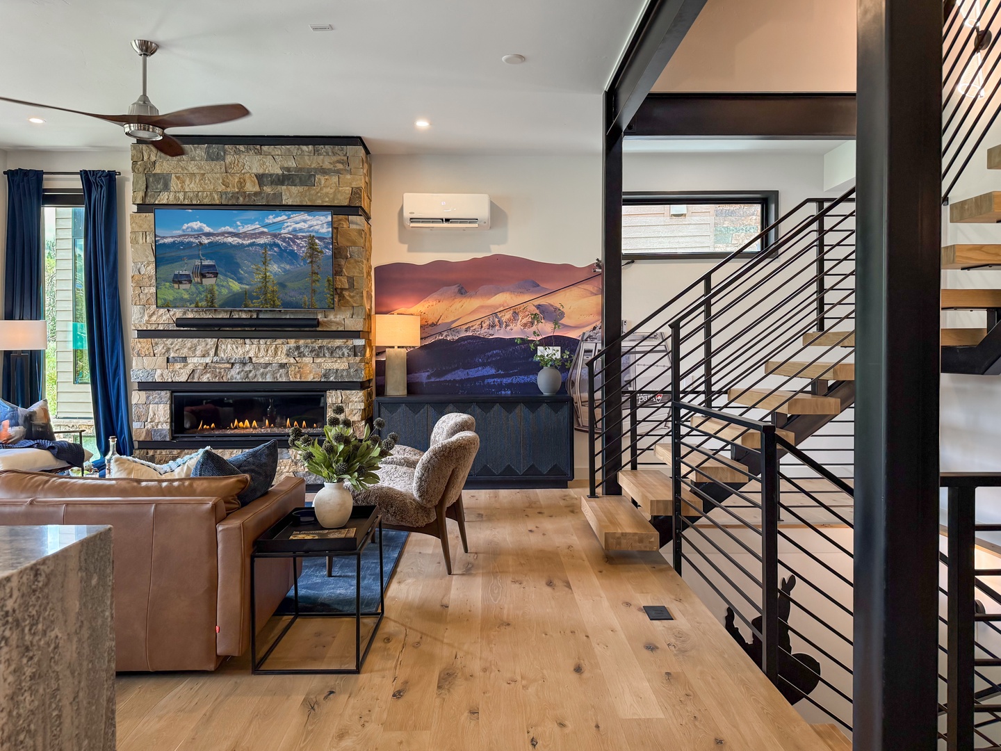 Unwind in your open-concept living space where modern mountain style meets cozy comfort. Sink into plush leather seating beside the stone fireplace while natural light fills the room through floor-to-ceiling windows.