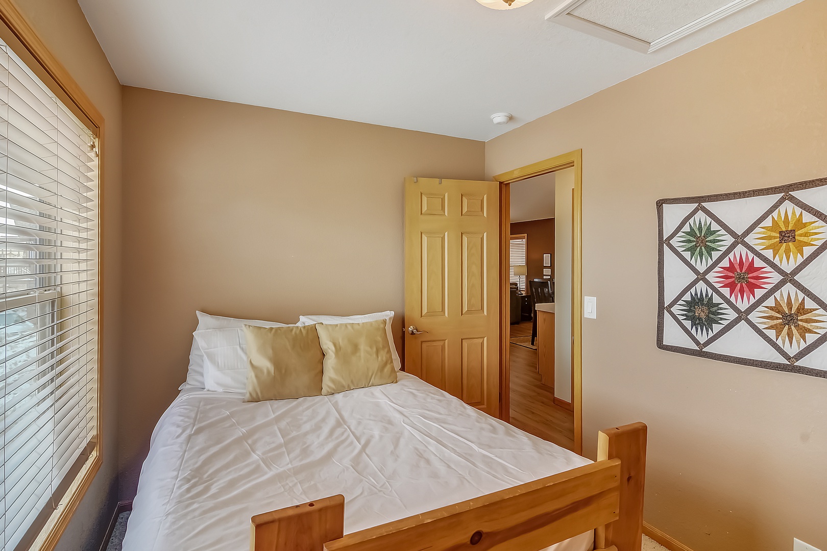 Unwind in your cozy bedroom featuring warm wood accents, crisp linens, and charming quilt artwork creating a peaceful retreat.