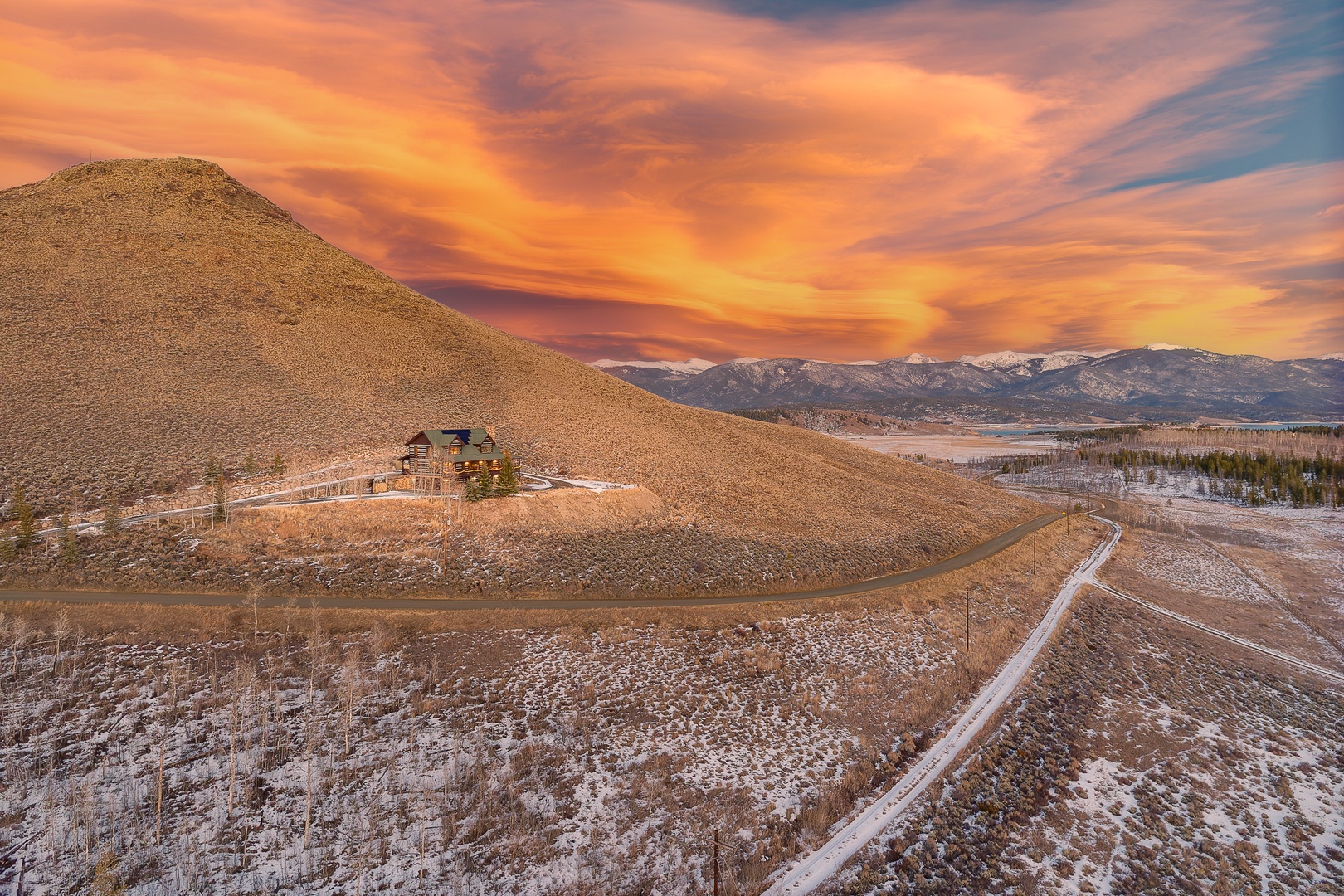 Stunning sunset paints the sky orange above this secluded mountain retreat, nestled on rolling hills with distant peaks.