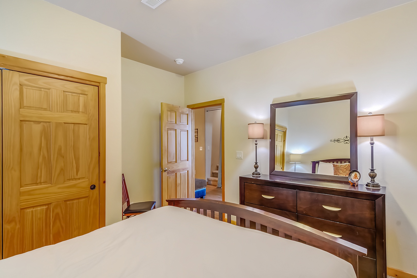 Relax in your comfortable bedroom featuring warm wood furnishings, elegant dresser with mirror, and thoughtful lighting for a cozy retreat.