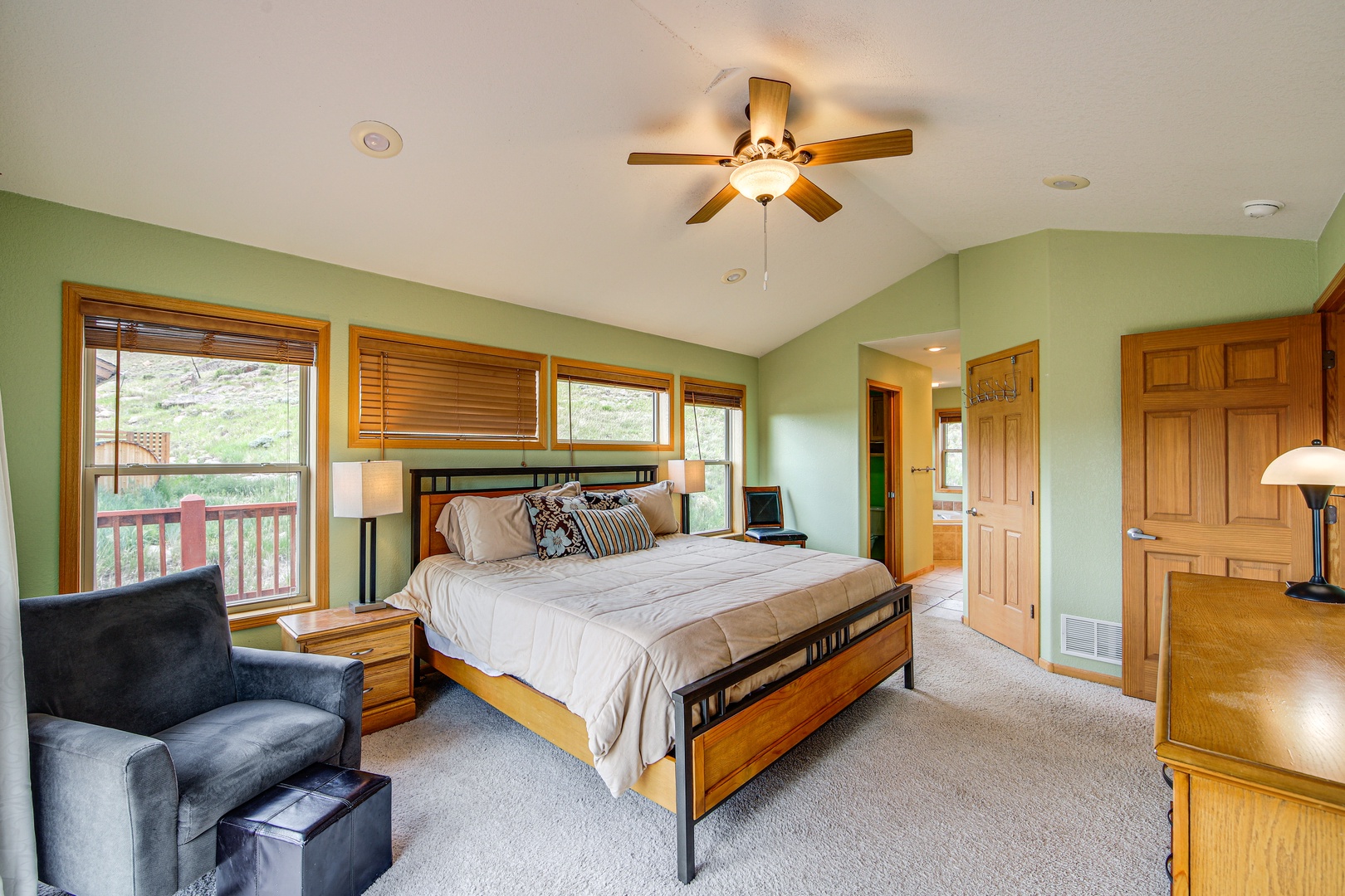 Drift off in your spacious bedroom featuring soothing green walls, warm wood accents, and a ceiling fan for perfect comfort.