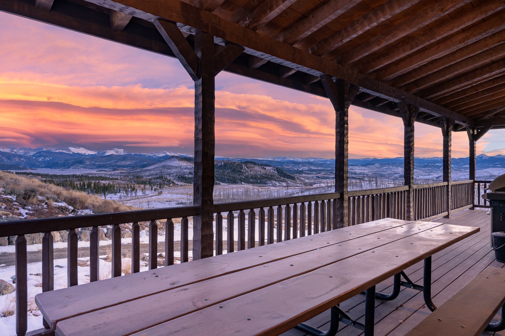 Expansive covered deck showcases breathtaking mountain sunset views across snow-dusted peaks and valleys.