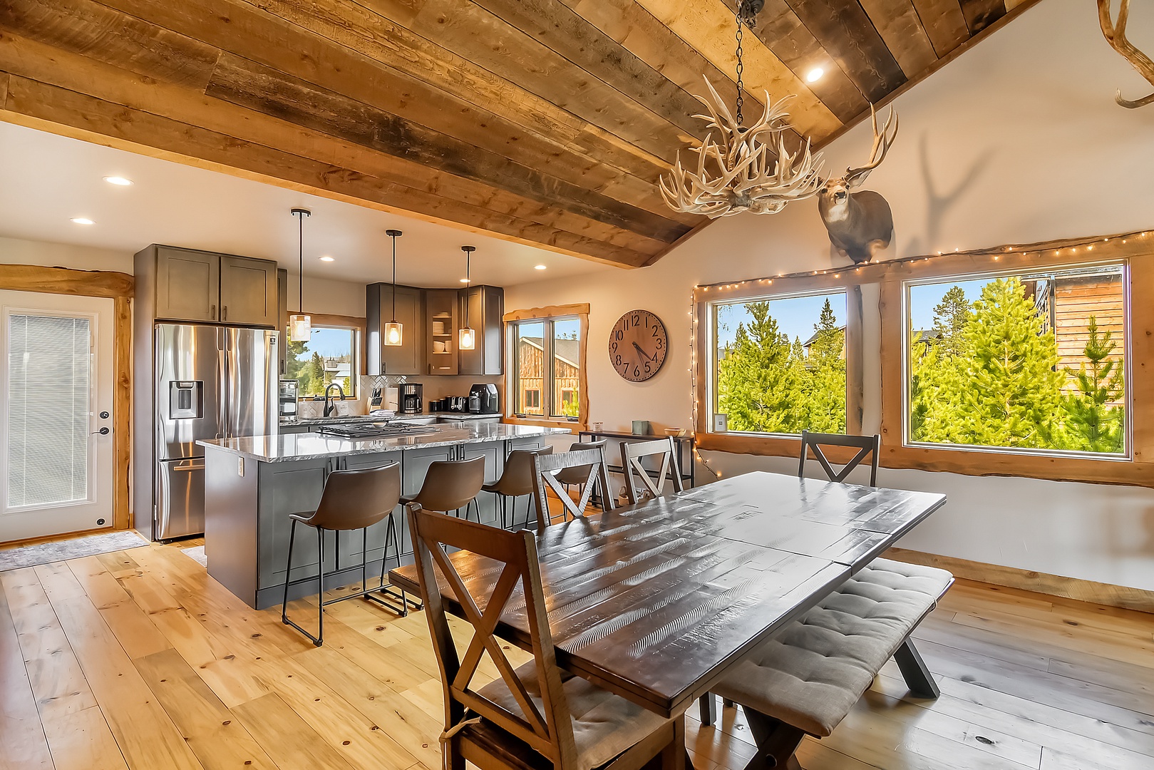 Gather around this stunning rustic dining space with exposed beams, modern kitchen, and forest views for memorable mountain meals together.