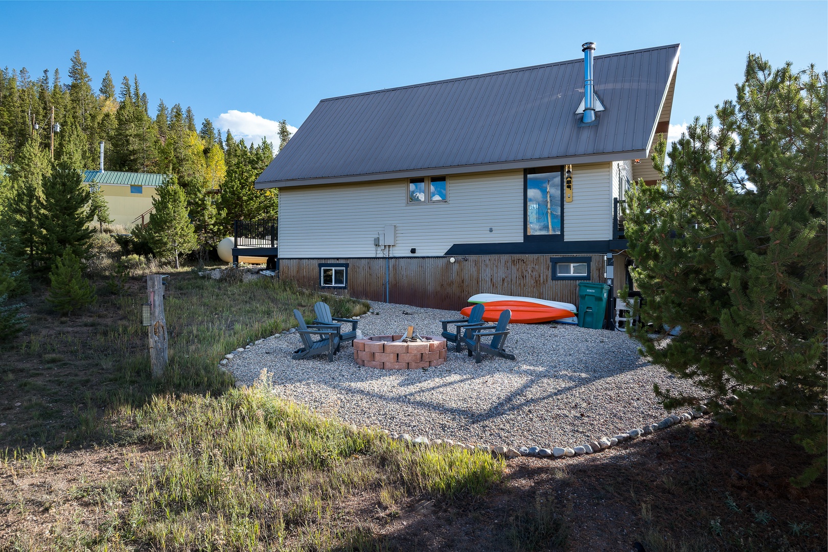 The property sits nestled among tall pines, offering a fire pit area with seating and kayak storage ready for your mountain adventures—a perfect basecamp in a natural, peaceful setting.