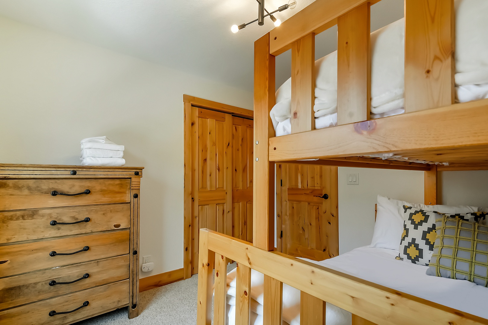 Your private bunk room offers sturdy wood-crafted beds with crisp linens, cheerful patterned pillows, and a roomy dresser for all your belongings—perfect for a cozy night's rest.