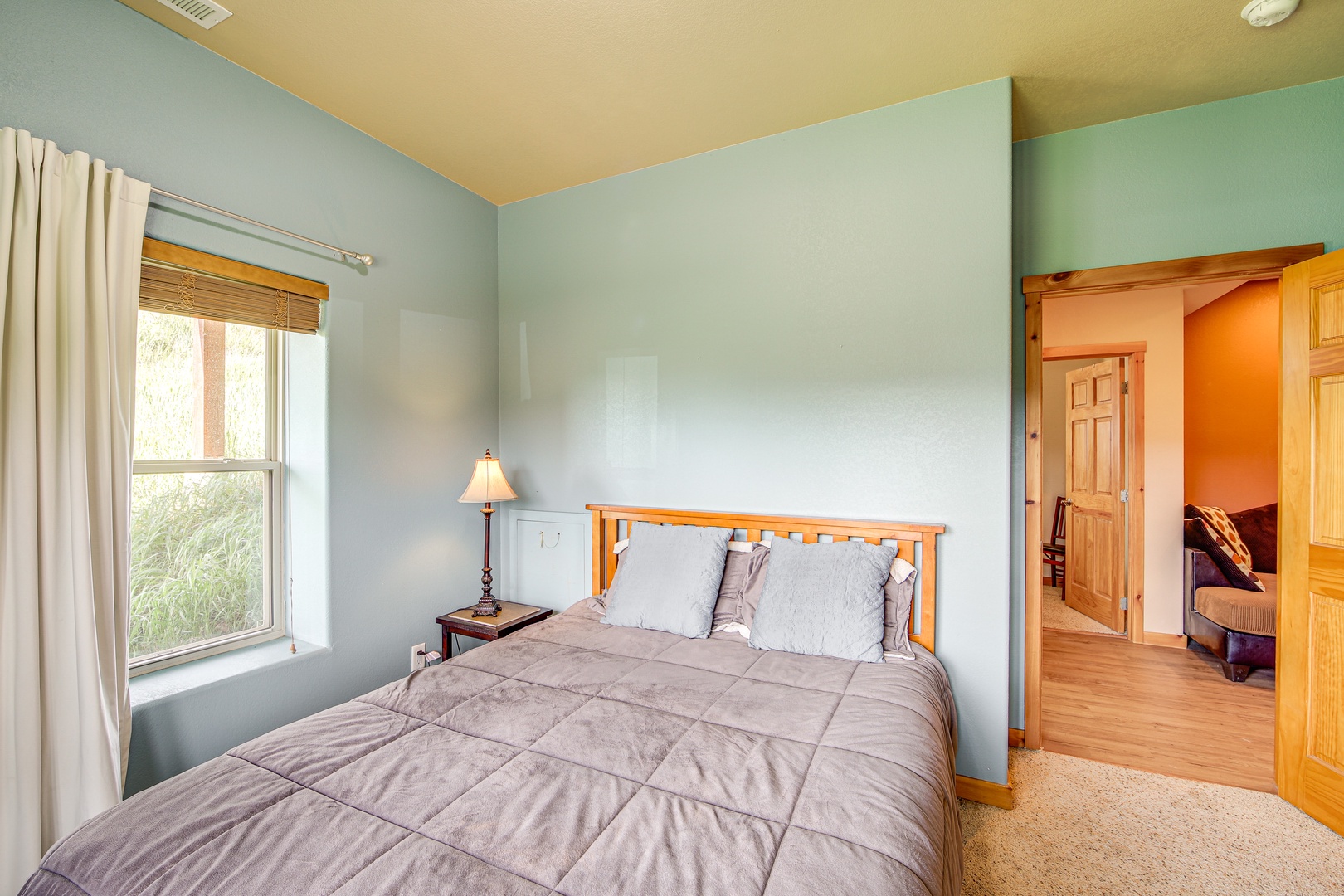 Drift into peaceful slumber in your cozy bedroom with soft blue walls, warm wood accents, and natural light streaming through charming windows.