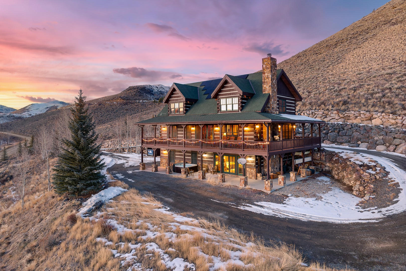 Stunning mountain lodge nestled in rugged terrain with snow-dusted hills and dramatic sunset skies creating a breathtaking alpine setting.