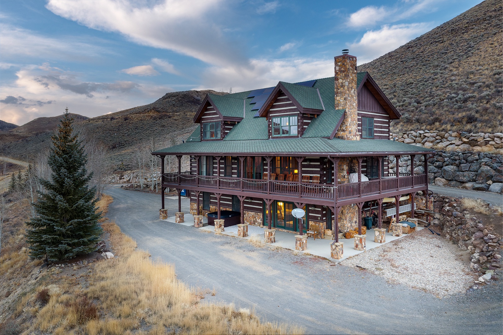Rustic mountain lodge nestled in rolling hills with stone chimney and wraparound balconies against dramatic sky.