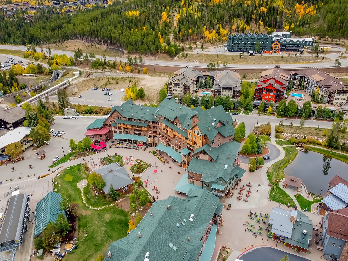 Aerial view of a mountain resort property surrounded by vibrant autumn foliage and neighboring lodges in a scenic mountain village setting.