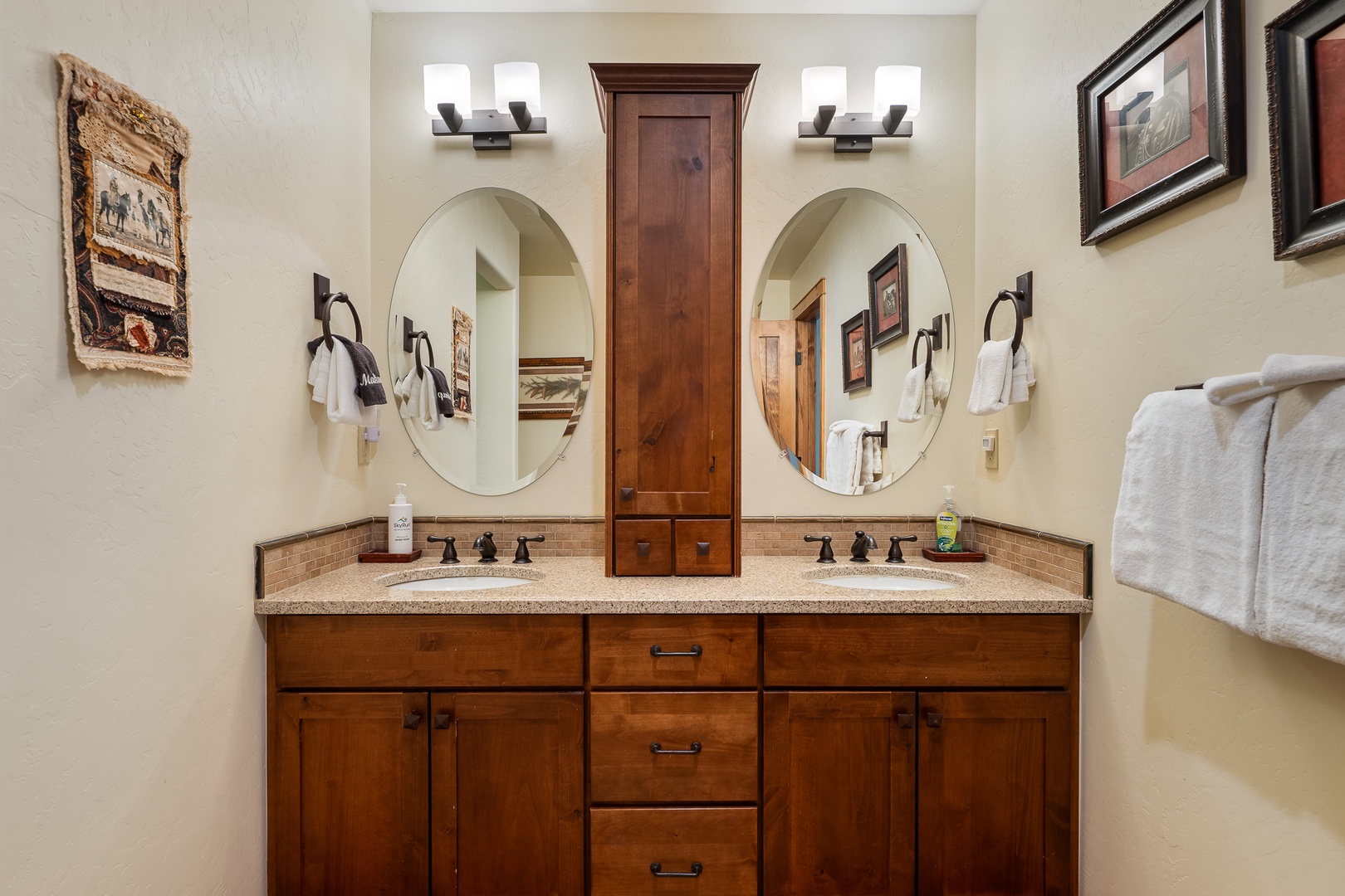 Step into your elegant dual-sink bathroom featuring warm wood cabinetry, round mirrors, and thoughtful artwork that creates a spa-like retreat.