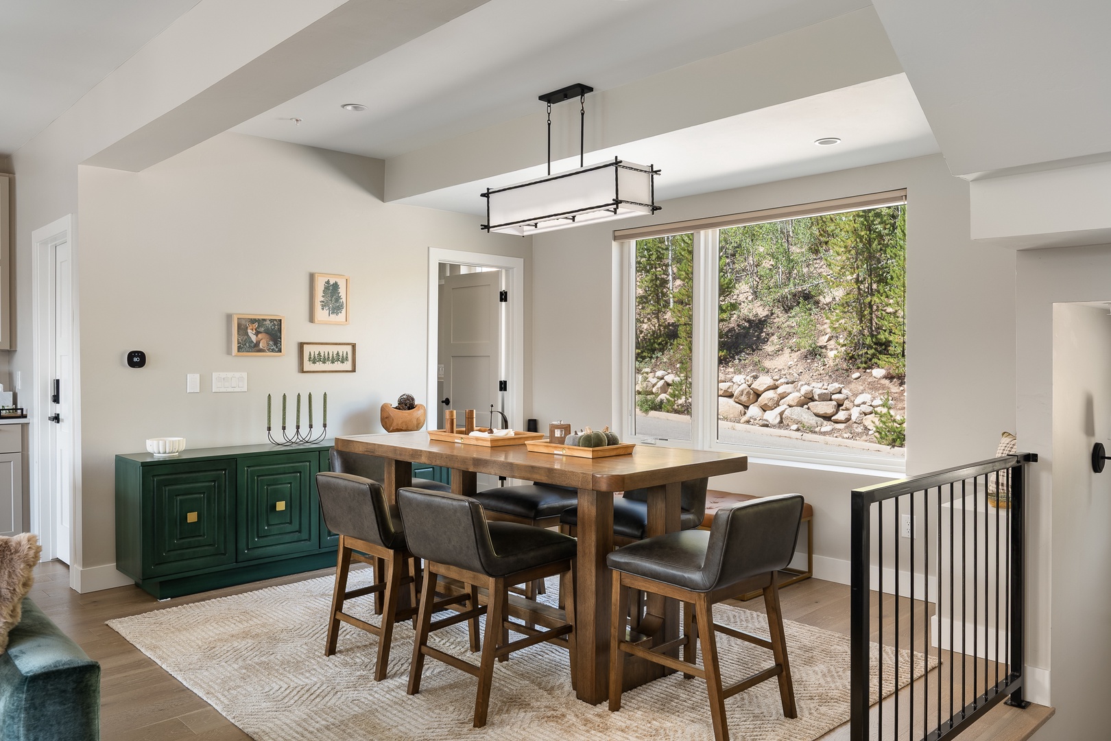 Gather around this inviting dining table with natural light streaming through floor-to-ceiling windows, where your mountain getaway meals become memorable moments against a peaceful hillside backdrop.