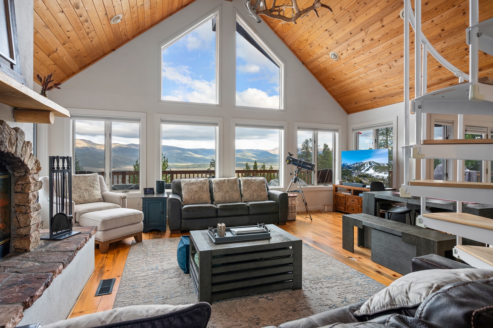 Sink into plush seating and gaze through soaring windows at stunning mountain vistas stretching beyond your private deck. The warm wood ceiling and stone fireplace create the perfect retreat after exploring.