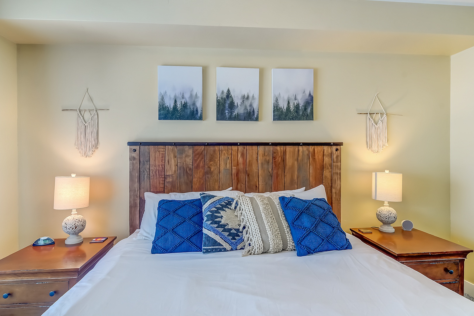 Sink into crisp white linens and plush blue pillows beneath forest artwork. Warm bedside lamps create perfect reading light for your mountain retreat.