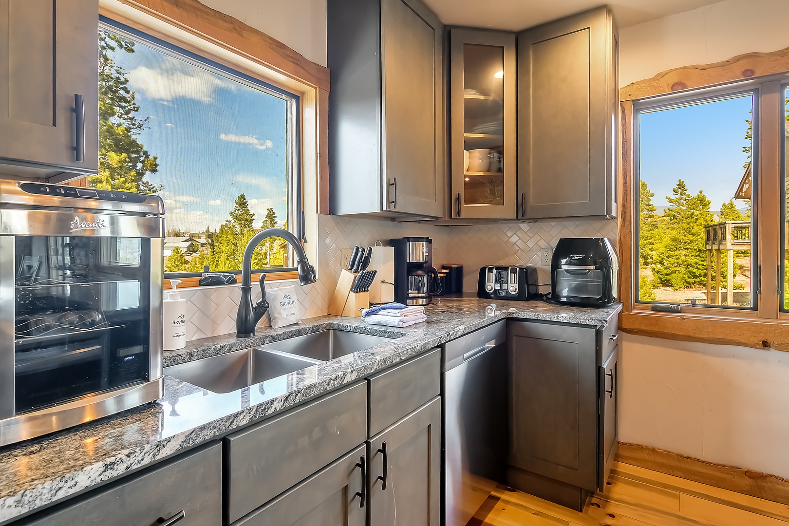 Your fully equipped kitchen features granite counters and forest views through large windows, perfect for morning coffee rituals.