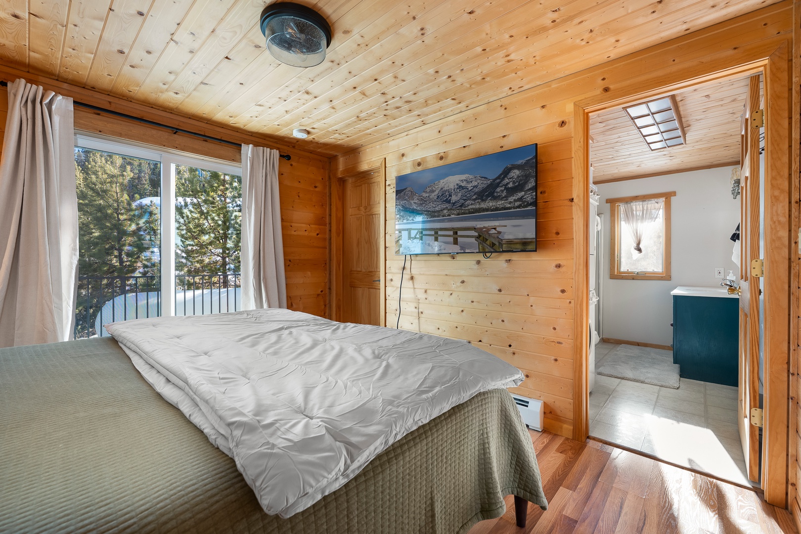 Unwind in your cozy alpine bedroom with warm wood walls, lake views through large windows, and a stunning mountain scene on TV to complete your mountain getaway.