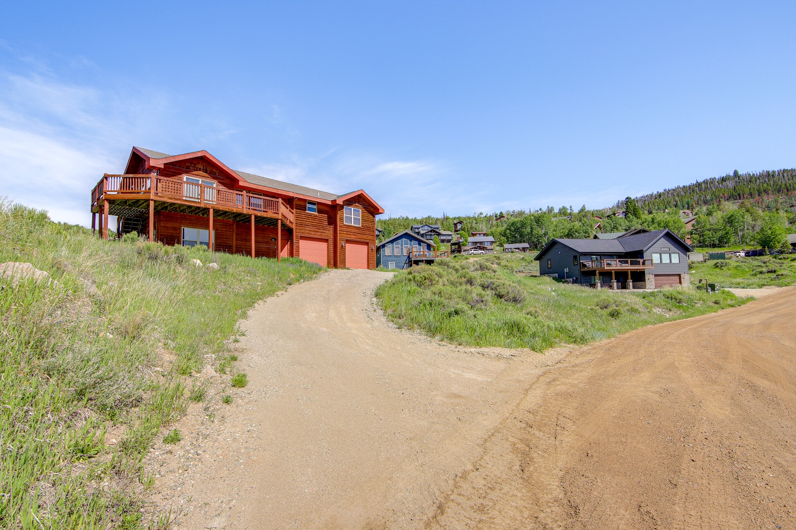 Mountain retreat featuring striking red cabin architecture surrounded by natural landscape and neighboring properties in peaceful hillside setting.