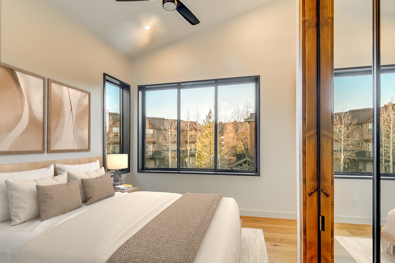 Sink into plush bedding while natural light streams through expansive windows, offering peaceful neighborhood views from your serene retreat.