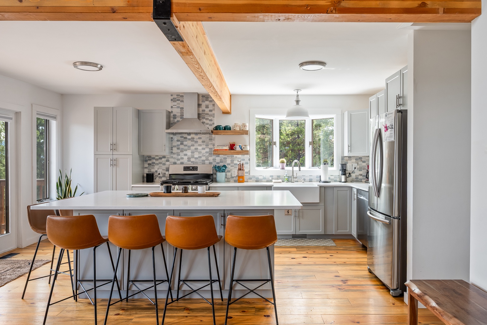 Gather around the spacious island in your bright, modern kitchen. Natural light pours through large windows, illuminating sleek countertops and warm wood beams overhead—perfect for cooking, chatting, and making memories.