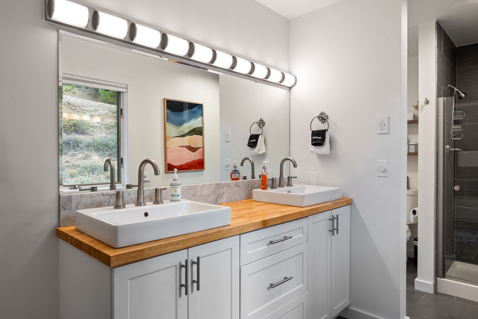 Step into your pristine bathroom featuring dual vessel sinks on a warm wooden countertop, perfect for getting ready together. Natural light filters through the window, while modern finishes make this space both stylish and functional.