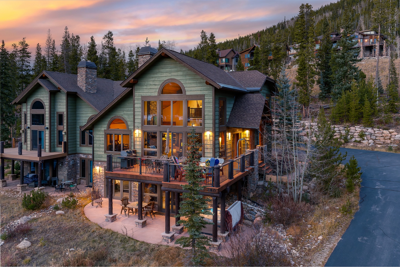 Mountain lodge retreat featuring stone and wood architecture with multiple decks overlooking forested slopes at twilight.