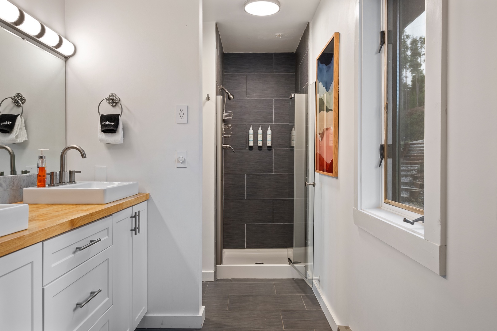 Your ensuite feels bright and modern, with a sleek glass-enclosed shower and dual sinks resting on warm wood counters—everything you need to refresh and recharge.