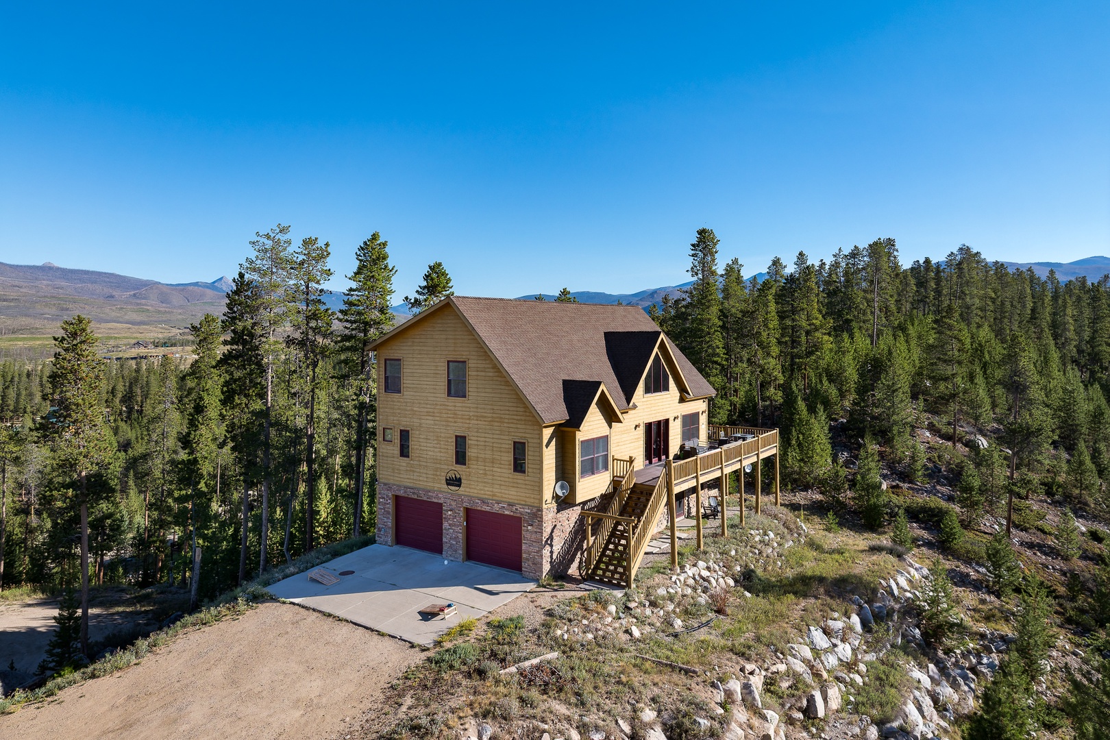 A mountain retreat nestled among evergreens, offering panoramic views of forested slopes and distant peaks under bright blue skies.