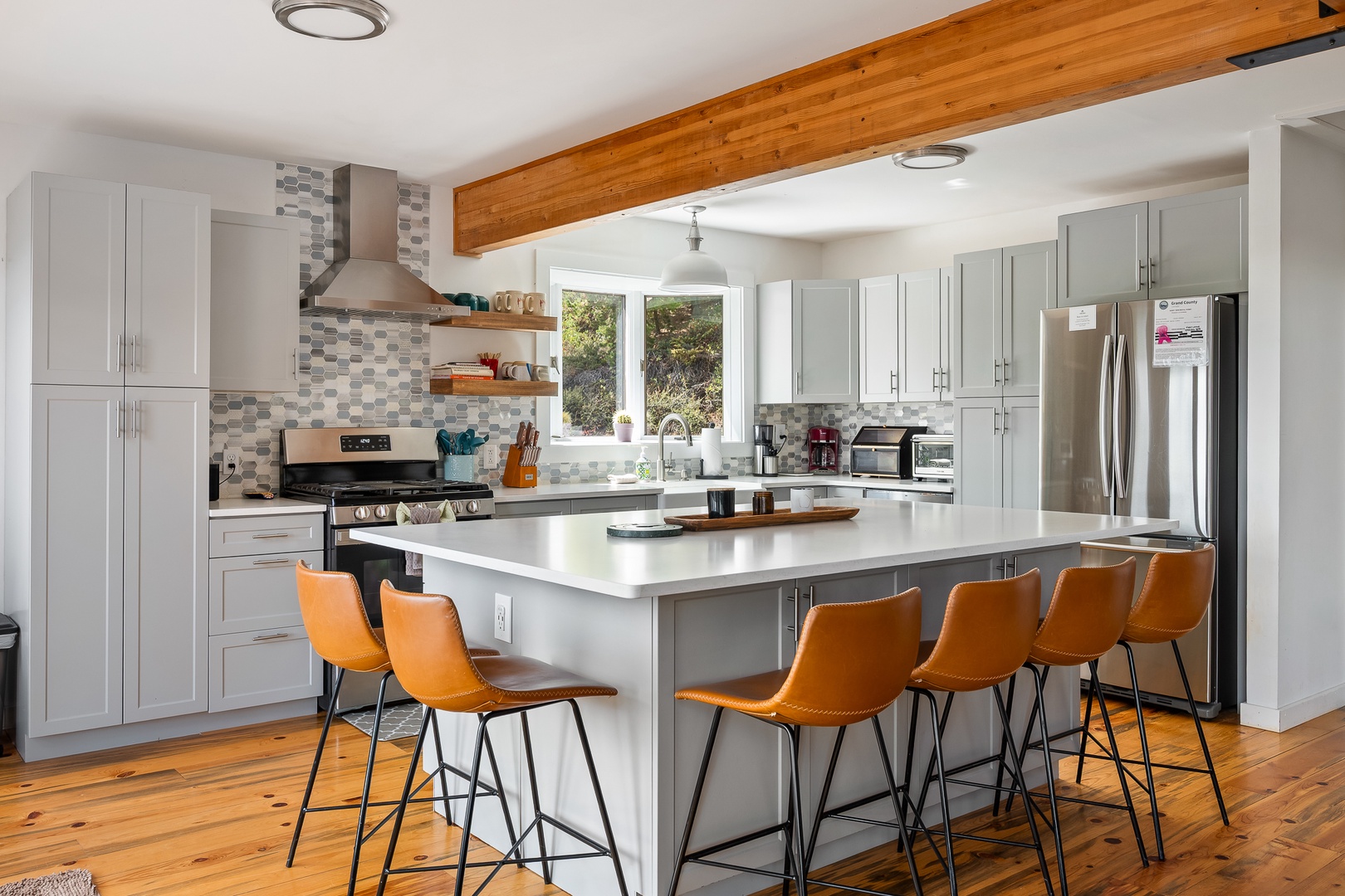 Gather around the spacious island where vibrant orange chairs invite you to enjoy morning coffee or share meals with loved ones in this bright, beautifully appointed kitchen with warm wood accents overhead.