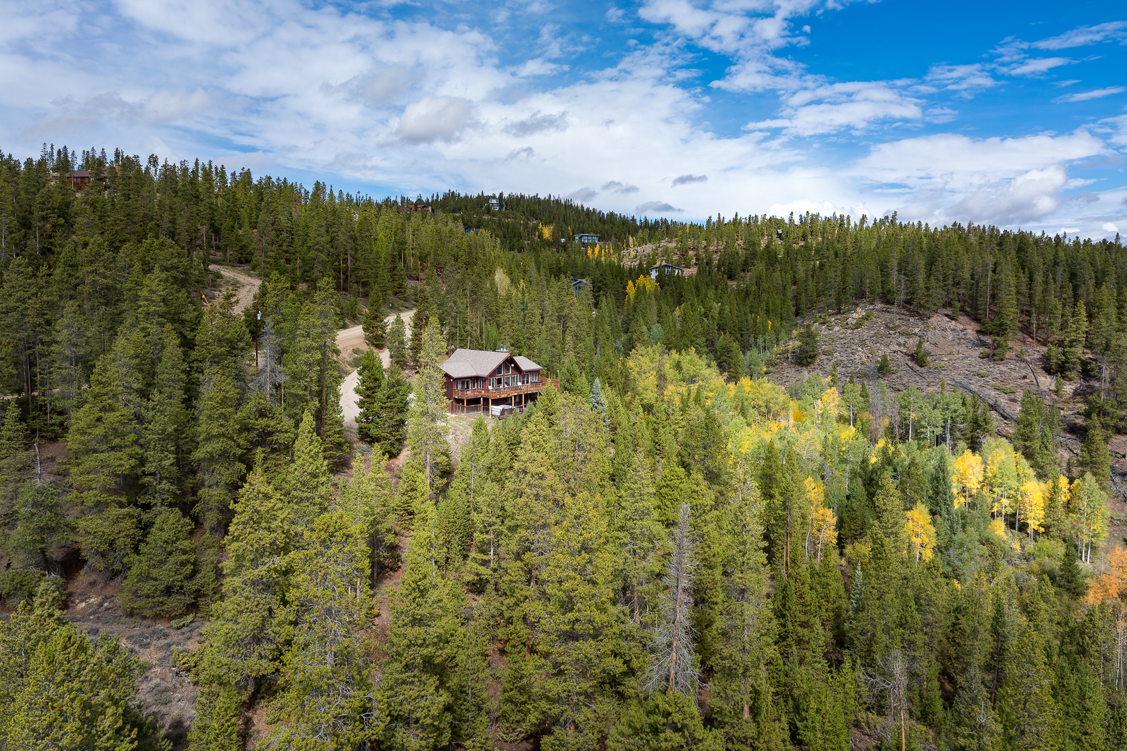 An aerial view of a secluded mountain cabin surrounded by evergreen forests and golden aspens, accessed by a private winding drive through pristine wilderness.