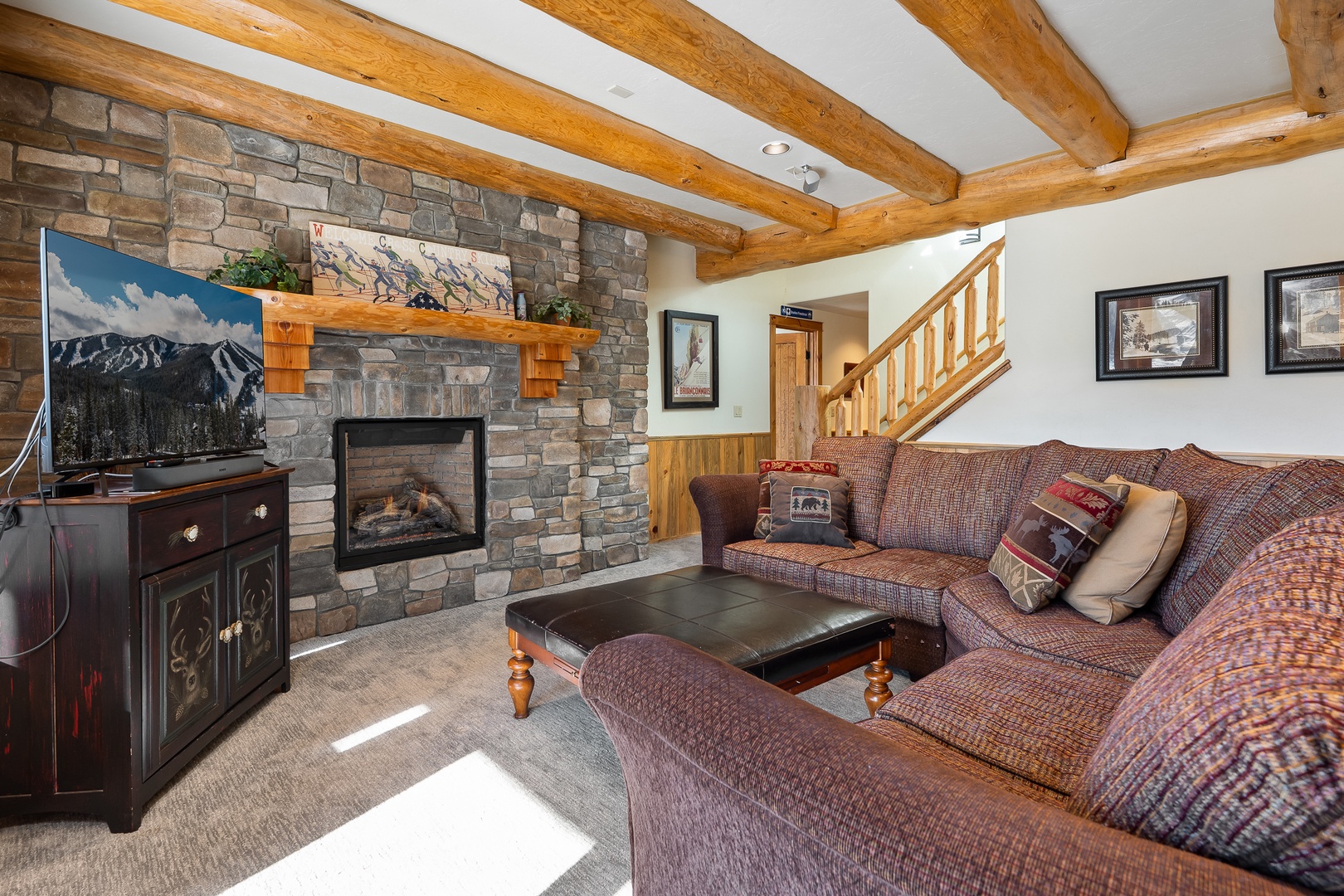 Downstairs stone fireplace under rustic beams, where plush seating and mountain views create the perfect retreat.