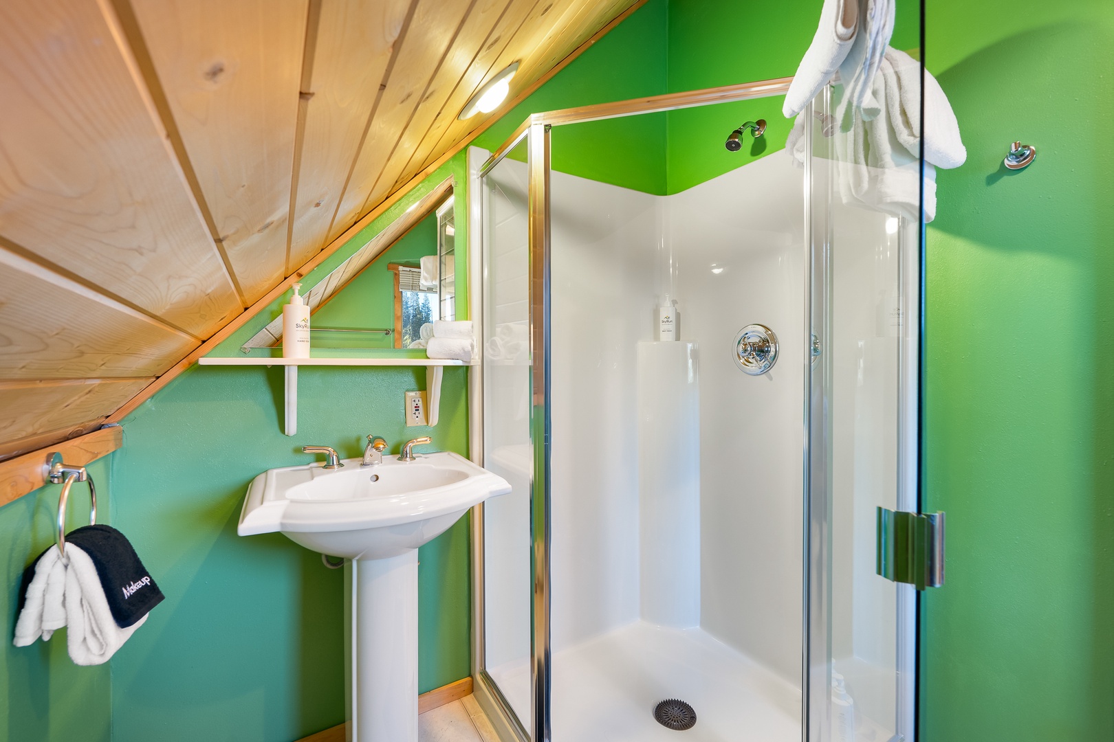 Refresh in your vibrant attic bathroom with modern glass shower and cheerful green walls under charming wooden beams.