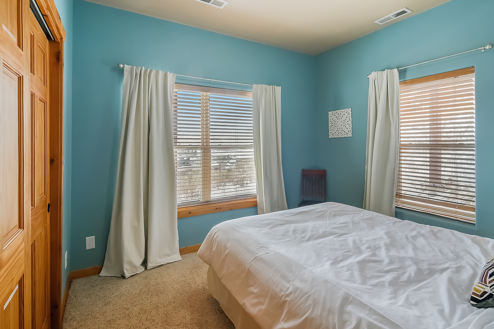 Drift off in your peaceful turquoise sanctuary with plush bedding and natural light streaming through wooden blinds.
