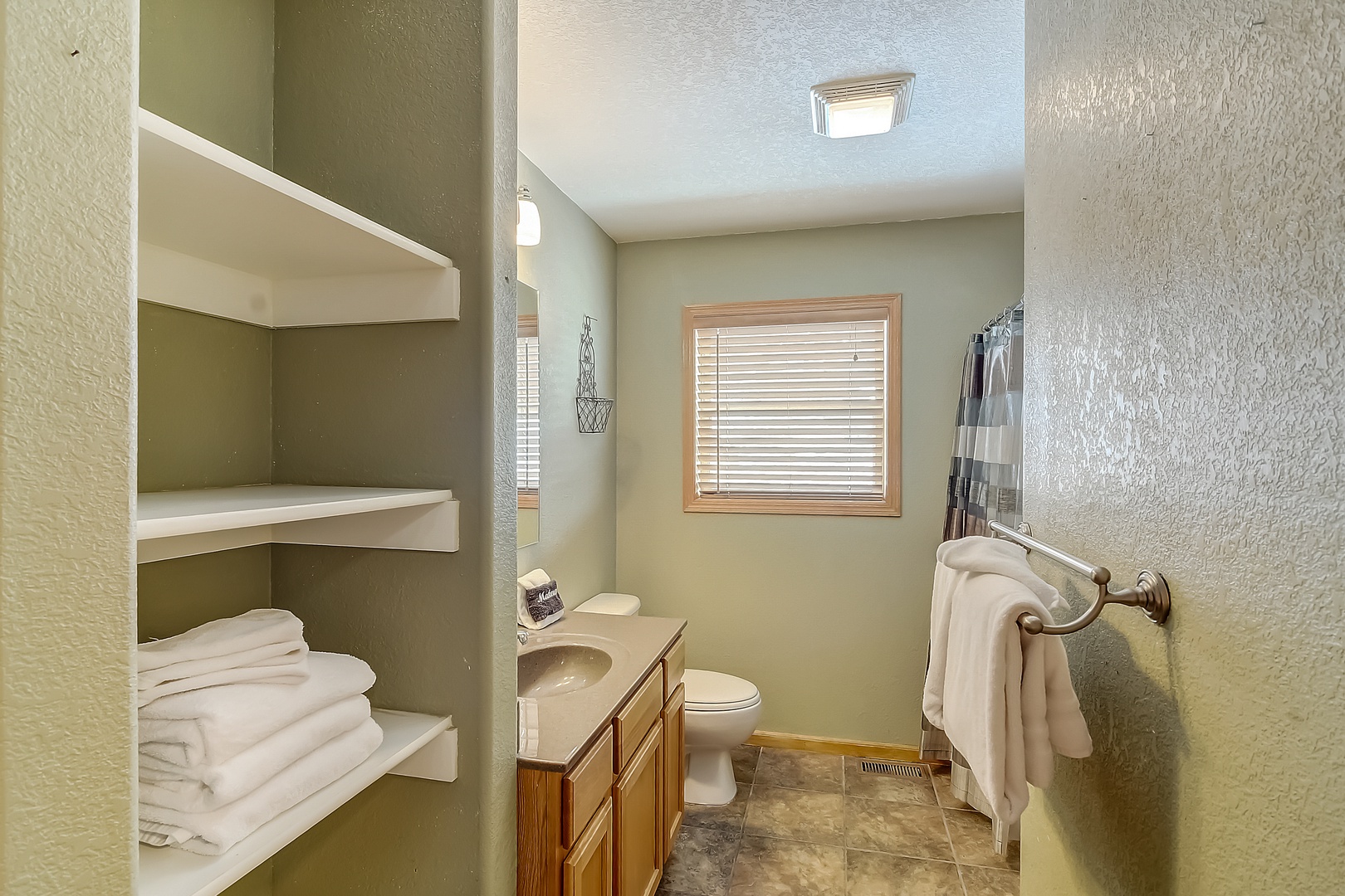 Step into your serene bathroom with plush towels waiting on built-in shelves and natural light streaming through wooden blinds.