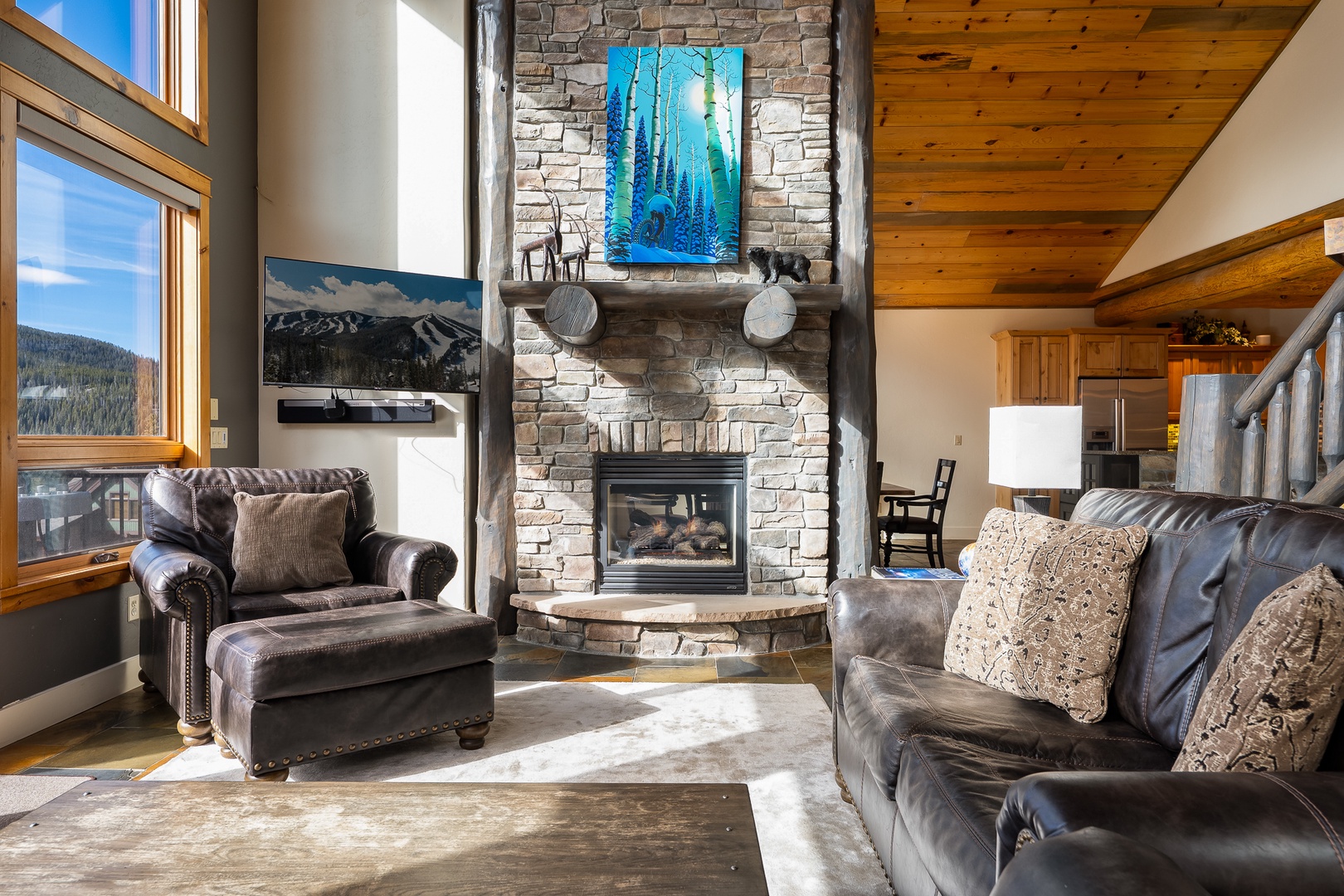 Cozy up in your mountain retreat's living room, where leather seating surrounds a stone fireplace and panoramic windows frame stunning views.