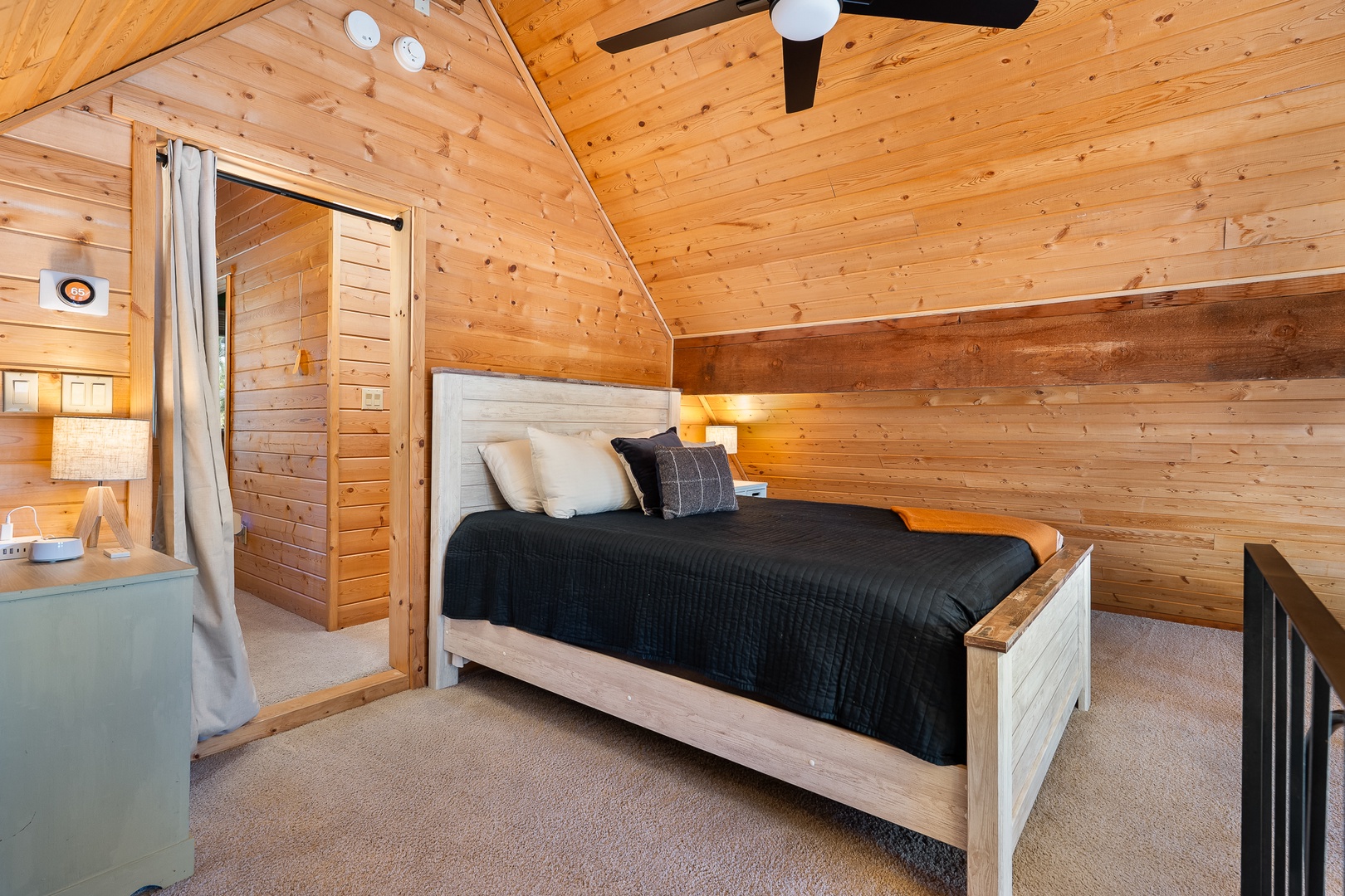 Your cozy loft bedroom awaits with warm wood beams, plush bedding, and rustic charm for peaceful mountain nights.