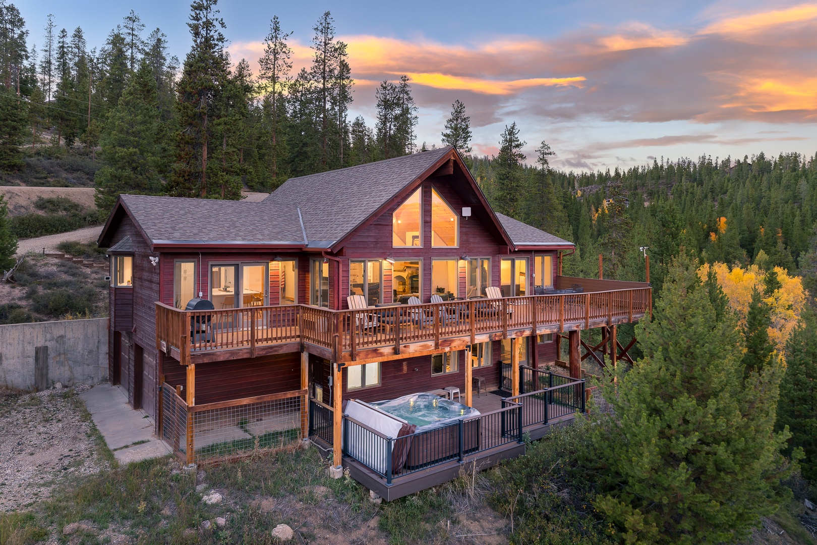 A mountain retreat surrounded by evergreen forests and golden aspens, featuring a private hot tub and spacious deck with stunning views at sunset.