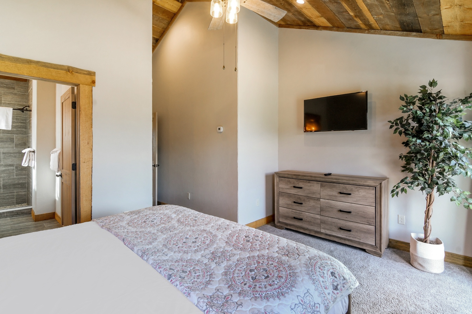Unwind in your spacious bedroom with rustic wooden beams, modern TV, and stylish dresser—your peaceful retreat awaits.