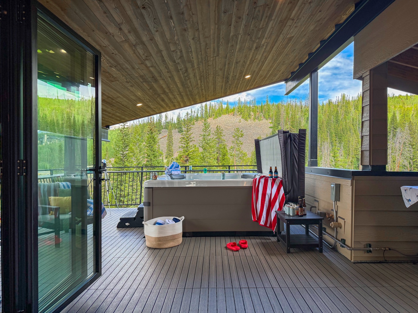 An outdoor deck framed by towering evergreen mountains, creating a peaceful retreat where you can soak in natural hot springs under open skies.