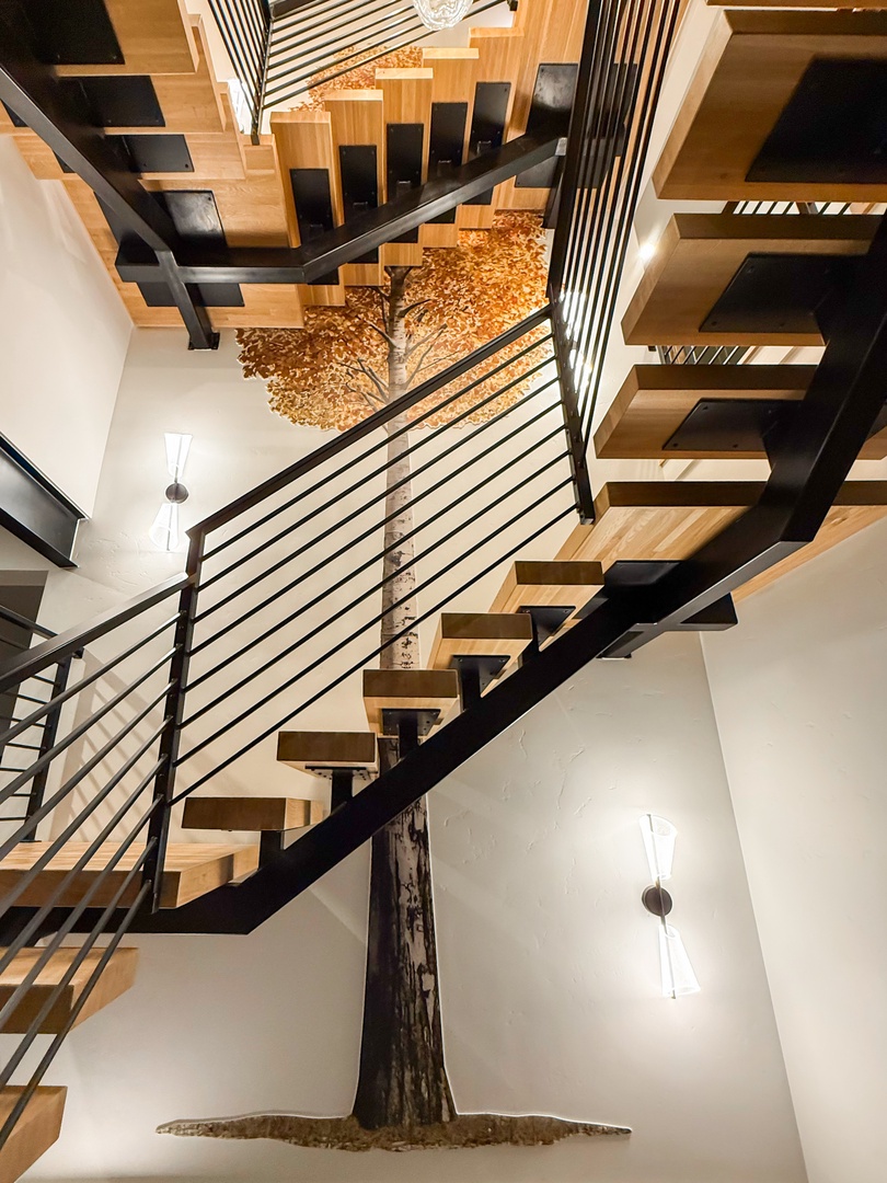 A striking staircase showcases modern wood and metal design, while a stunning decorative tree installation anchors the soaring space with natural artistry.